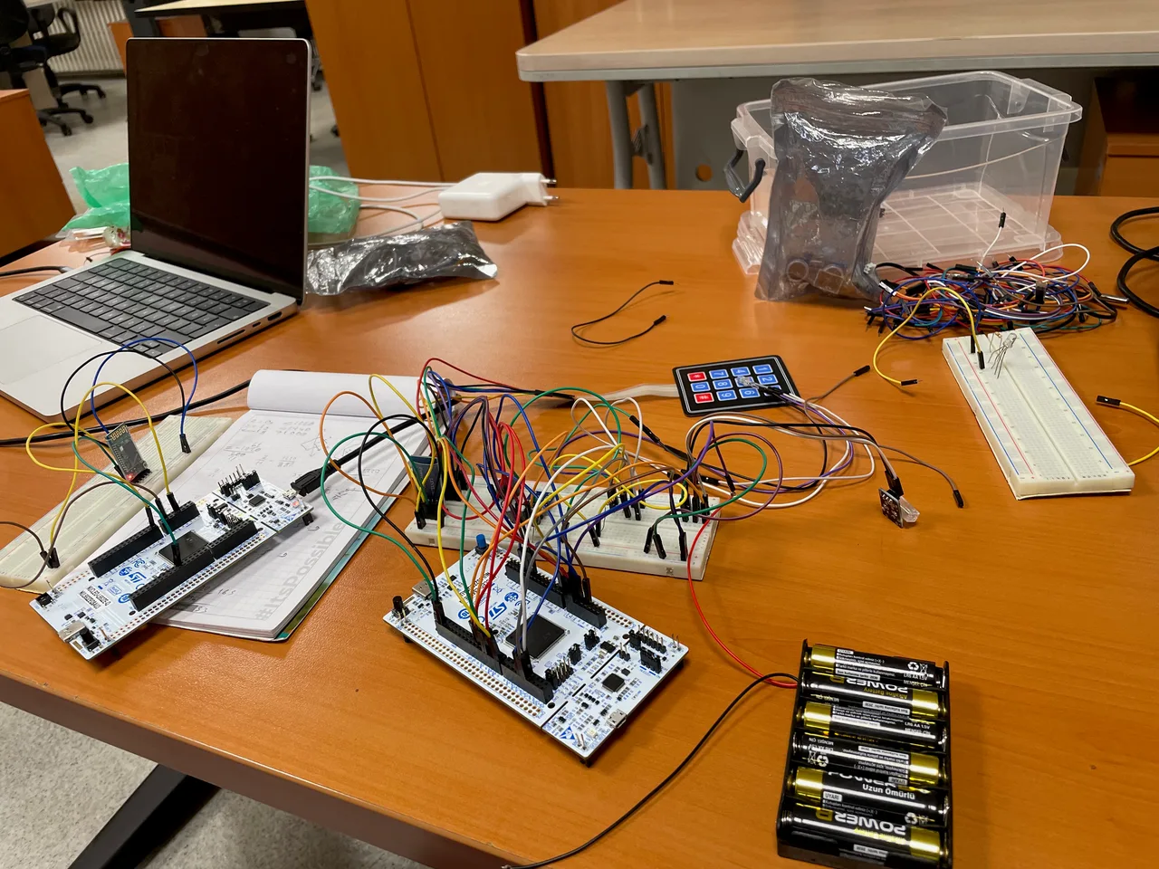 The development workbench with STM32 Nucleo boards, a Bluetooth module, breadboards, keypad, and battery pack.